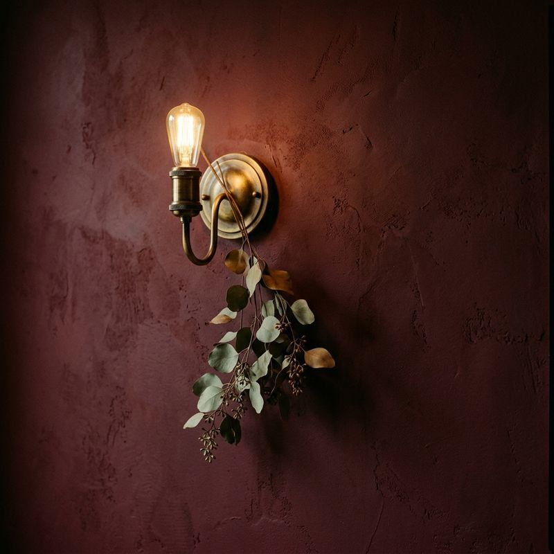 A brass sconce and dried eucalyptus on a deep maroon wall